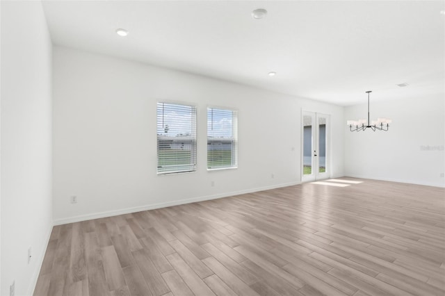 empty room with french doors, baseboards, light wood finished floors, and an inviting chandelier