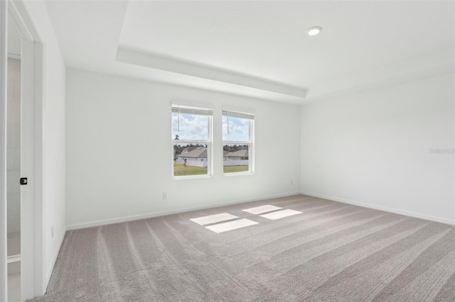 carpeted spare room featuring a tray ceiling and baseboards