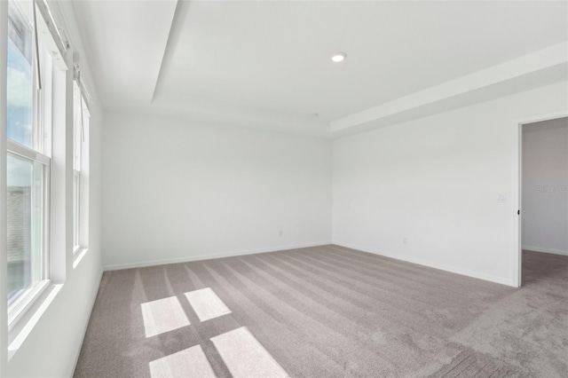 carpeted spare room featuring recessed lighting, a raised ceiling, and baseboards