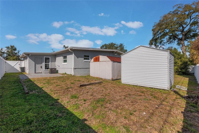 rear view of house featuring a patio, a yard, central AC unit, and a storage unit