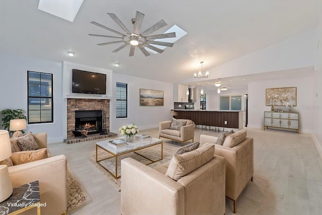 living room with an inviting chandelier, a brick fireplace, lofted ceiling with skylight, and light hardwood / wood-style floors