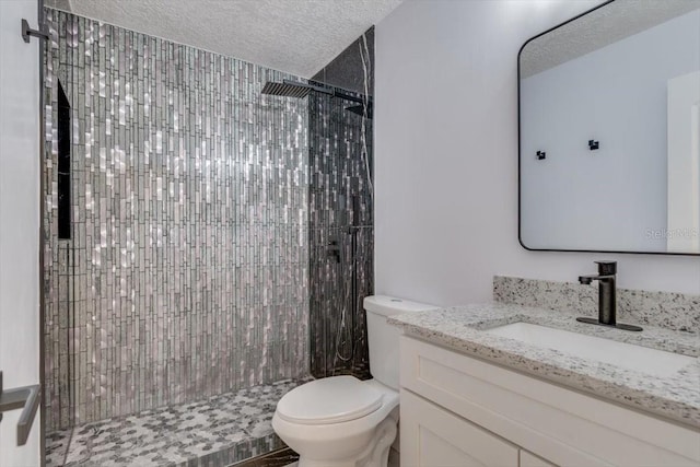 bathroom with vanity, tiled shower, a textured ceiling, and toilet