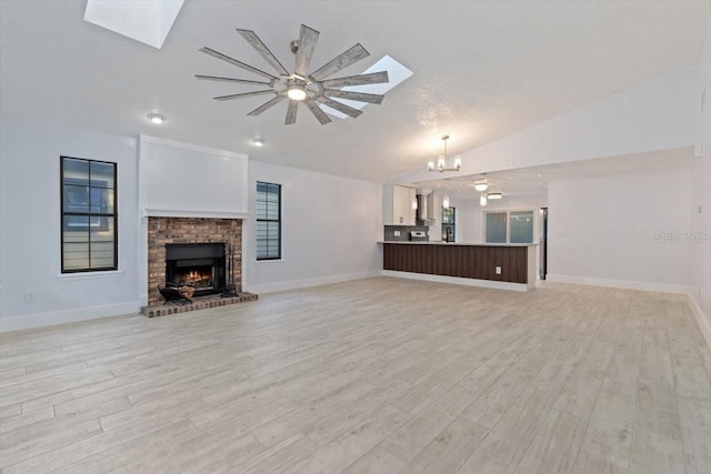 unfurnished living room featuring lofted ceiling with skylight, a fireplace, an inviting chandelier, and light hardwood / wood-style flooring