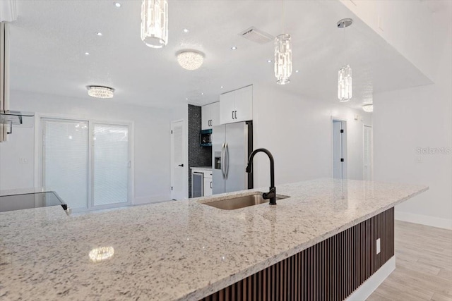 kitchen featuring stainless steel refrigerator with ice dispenser, decorative light fixtures, light stone countertops, and sink