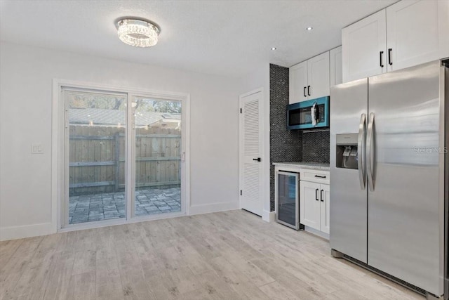 kitchen featuring appliances with stainless steel finishes, beverage cooler, light hardwood / wood-style flooring, and white cabinets