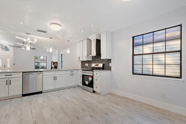 kitchen with wall chimney exhaust hood, hanging light fixtures, stainless steel appliances, decorative backsplash, and white cabinets