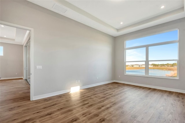 spare room with a water view, a tray ceiling, and hardwood / wood-style flooring