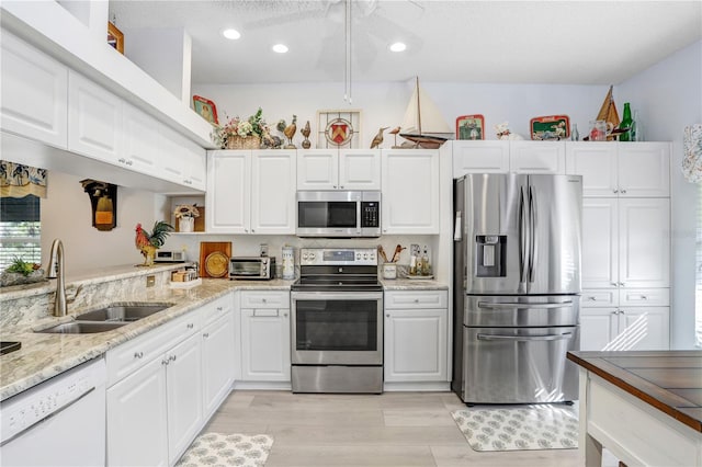 kitchen featuring sink, white cabinetry, light wood-type flooring, stainless steel appliances, and light stone countertops