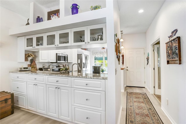 bar featuring white cabinetry, light stone counters, stainless steel appliances, and light wood-type flooring