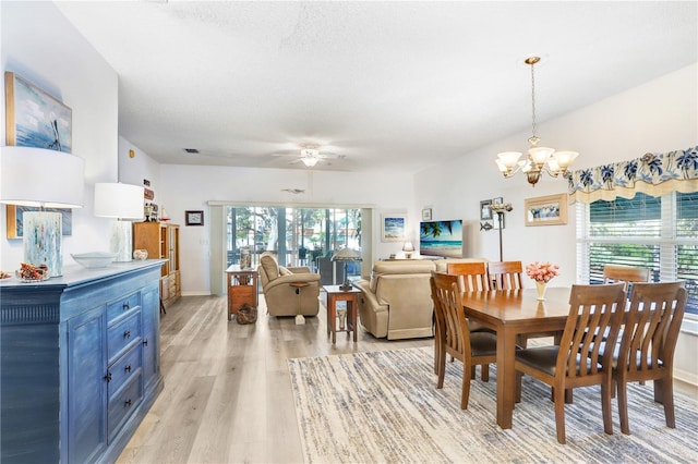 dining space with ceiling fan with notable chandelier, a textured ceiling, and light wood-type flooring