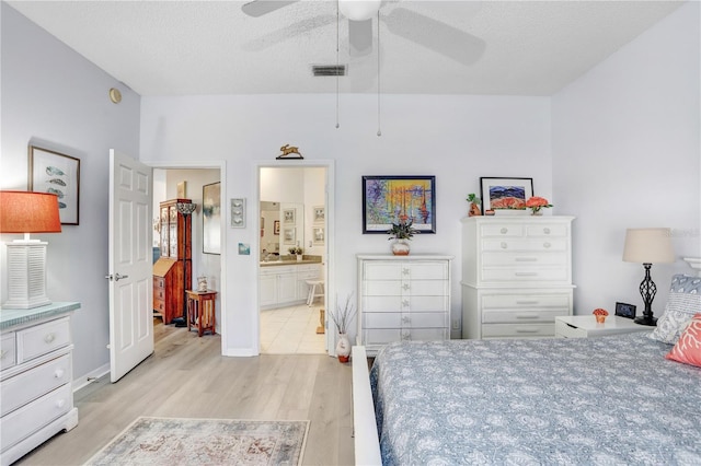 bedroom with ceiling fan, ensuite bath, light hardwood / wood-style flooring, and a textured ceiling