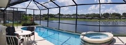 view of swimming pool with an in ground hot tub, a water view, glass enclosure, and a patio