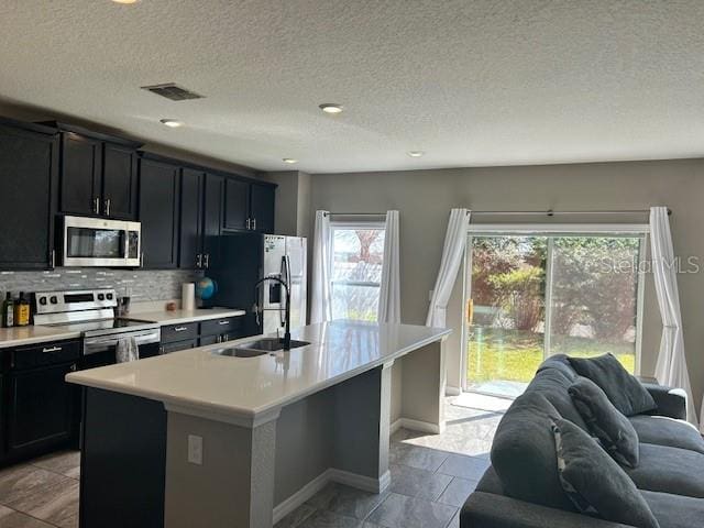 kitchen with tasteful backsplash, sink, a center island with sink, and appliances with stainless steel finishes