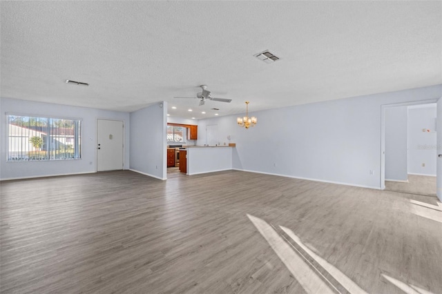 unfurnished living room with hardwood / wood-style flooring, a healthy amount of sunlight, ceiling fan with notable chandelier, and a textured ceiling