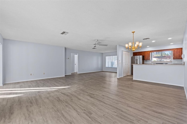 unfurnished living room with ceiling fan with notable chandelier, light hardwood / wood-style flooring, and a textured ceiling