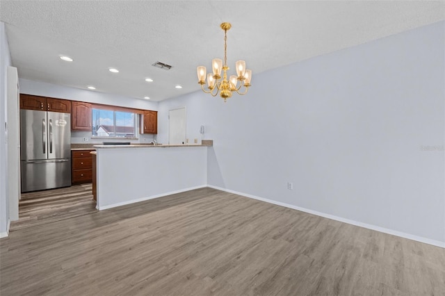 kitchen with hanging light fixtures, wood-type flooring, stainless steel fridge, and kitchen peninsula