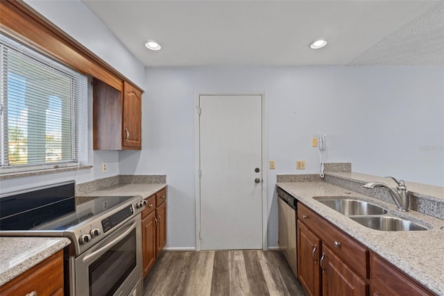 kitchen with appliances with stainless steel finishes, sink, dark wood-type flooring, and light stone counters