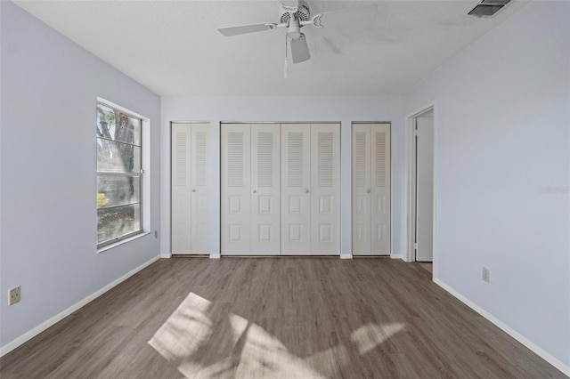 unfurnished bedroom featuring multiple closets, ceiling fan, hardwood / wood-style floors, and multiple windows