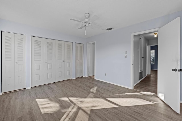 unfurnished bedroom featuring multiple closets, ceiling fan, and hardwood / wood-style flooring