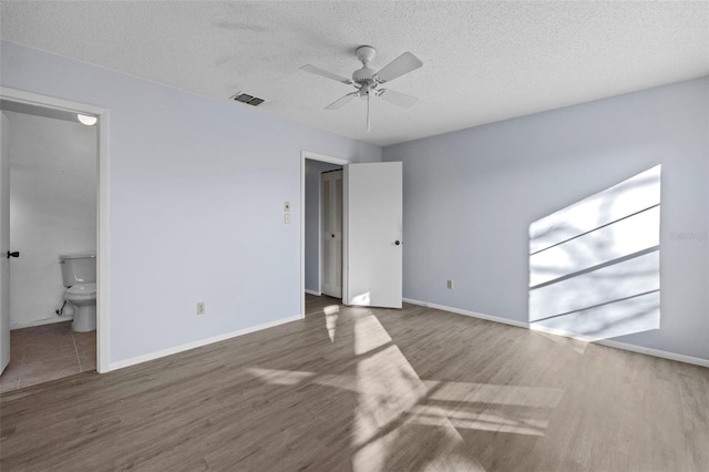 unfurnished bedroom with ensuite bath, dark hardwood / wood-style floors, and a textured ceiling