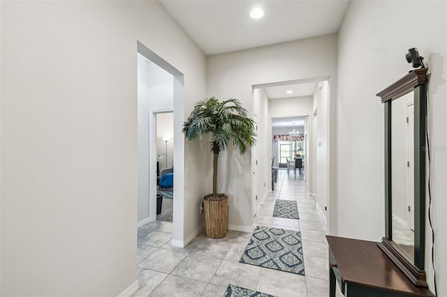 corridor featuring baseboards, an inviting chandelier, and light tile patterned flooring