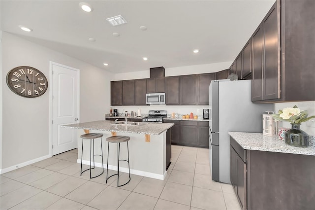 283 Archer Way, Haines City, FL 33844 - kitchen with dark brown cabinetry, sink, light stone counters, appliances with stainless steel finishes, and a kitchen island with sink