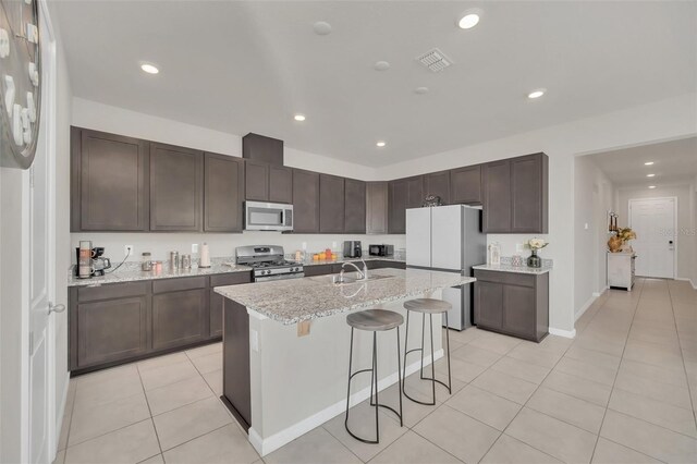 283 Archer Way, Haines City, FL 33844 - kitchen featuring sink, light tile patterned floors, stainless steel appliances, light stone countertops, and a center island with sink