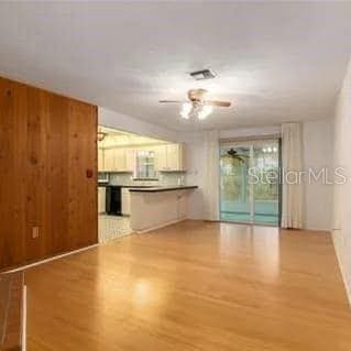 unfurnished living room featuring hardwood / wood-style flooring, wooden walls, and ceiling fan