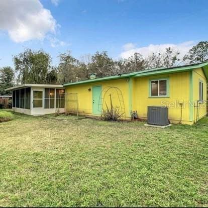 back of house featuring central AC unit, a lawn, and a sunroom