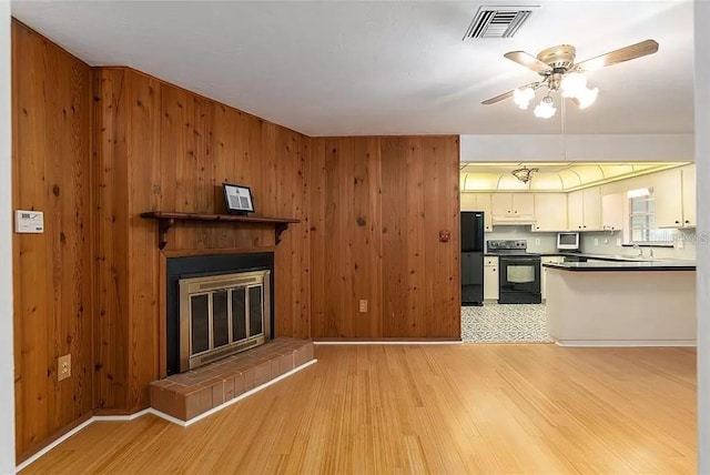 kitchen featuring a tiled fireplace, black appliances, white cabinets, and light wood-type flooring