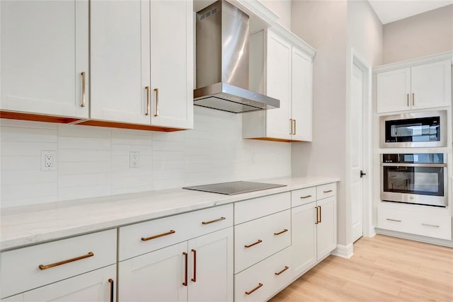 kitchen with stainless steel appliances, light stone countertops, wall chimney range hood, and white cabinets