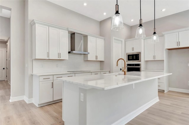 kitchen featuring a center island with sink, pendant lighting, wall chimney range hood, and white cabinets