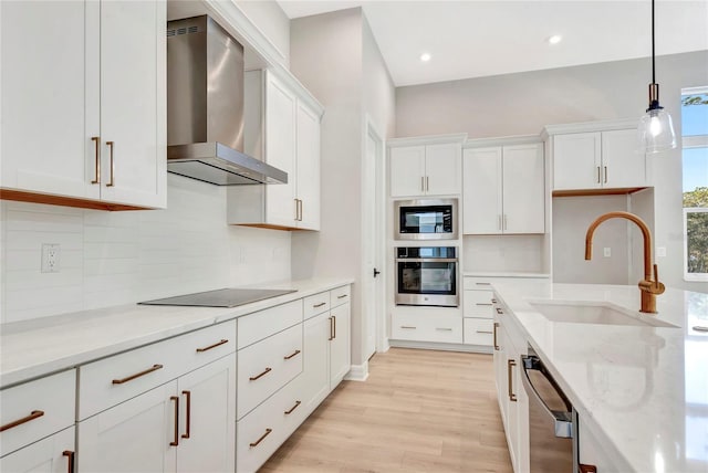 kitchen featuring wall chimney range hood, stainless steel appliances, sink, and white cabinets