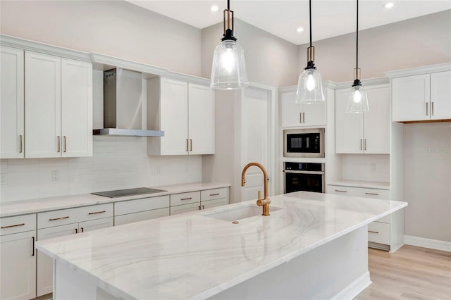 kitchen with wall chimney range hood, black appliances, an island with sink, and white cabinets