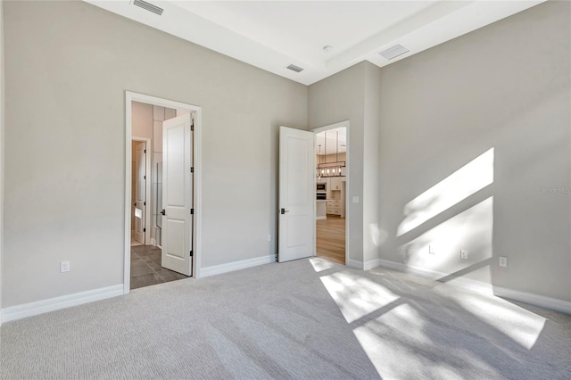 unfurnished bedroom featuring a high ceiling, ensuite bathroom, and carpet flooring