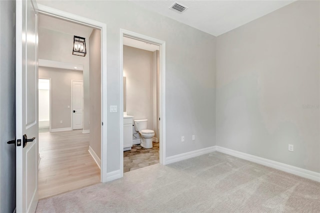 unfurnished bedroom featuring light colored carpet and ensuite bath