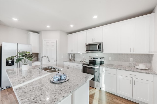 kitchen with appliances with stainless steel finishes, sink, white cabinets, light stone countertops, and a center island with sink