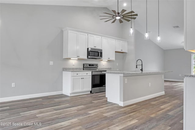 kitchen featuring appliances with stainless steel finishes, white cabinetry, light stone countertops, decorative light fixtures, and light wood-type flooring