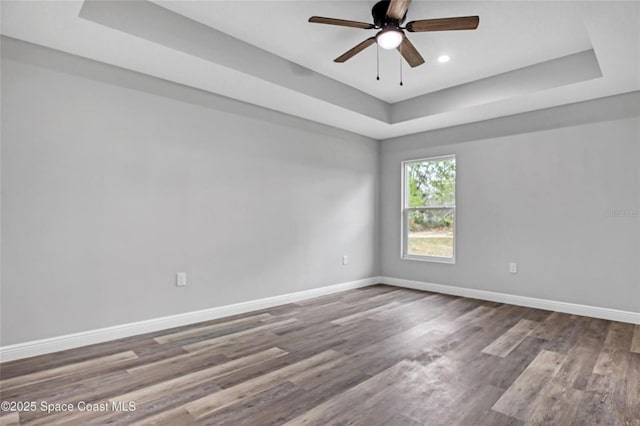 empty room featuring hardwood / wood-style flooring, ceiling fan, and a raised ceiling