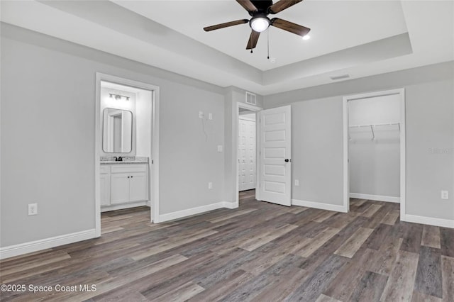 unfurnished bedroom featuring dark wood-type flooring, ensuite bath, a raised ceiling, and a closet