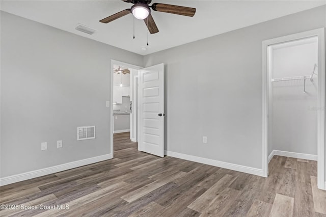 unfurnished bedroom featuring a spacious closet, hardwood / wood-style floors, ceiling fan, and a closet