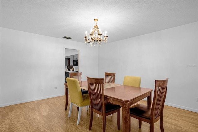 dining area featuring a textured ceiling, a notable chandelier, and light wood-type flooring