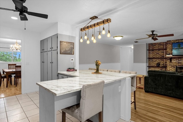 kitchen with light stone countertops, hanging light fixtures, a breakfast bar area, and light hardwood / wood-style flooring