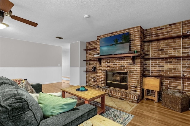 living room with ceiling fan, wood-type flooring, a fireplace, and a textured ceiling