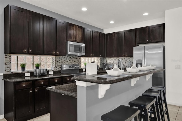 kitchen with appliances with stainless steel finishes, a kitchen island with sink, dark brown cabinetry, a kitchen bar, and decorative backsplash