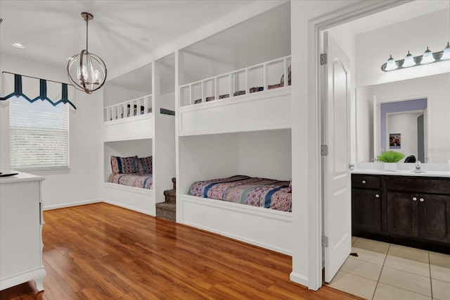 bedroom featuring ensuite bath, sink, light hardwood / wood-style floors, and a notable chandelier