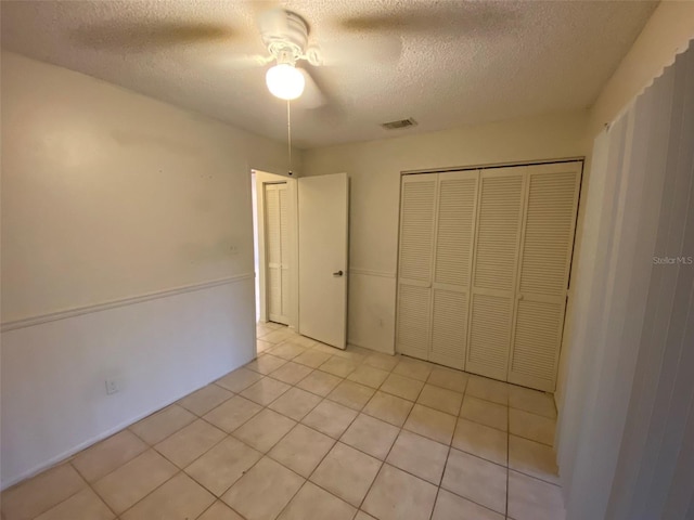 unfurnished bedroom featuring light tile patterned floors, ceiling fan, a textured ceiling, and a closet