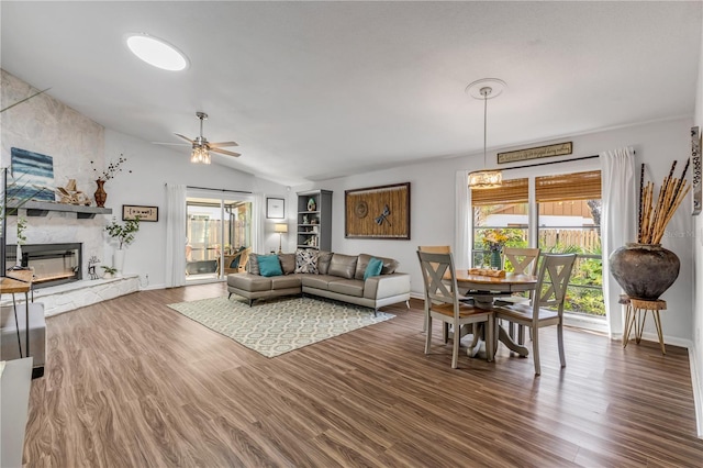 living room with hardwood / wood-style floors, a stone fireplace, vaulted ceiling, and ceiling fan with notable chandelier