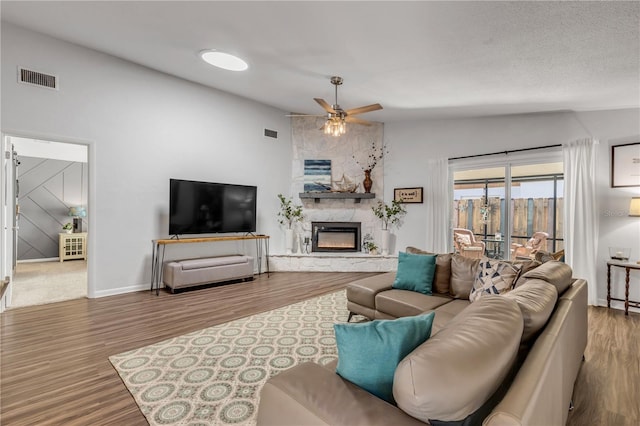 living room featuring lofted ceiling, hardwood / wood-style floors, a large fireplace, and ceiling fan