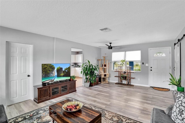 living room featuring ceiling fan, a barn door, a textured ceiling, and light wood-type flooring